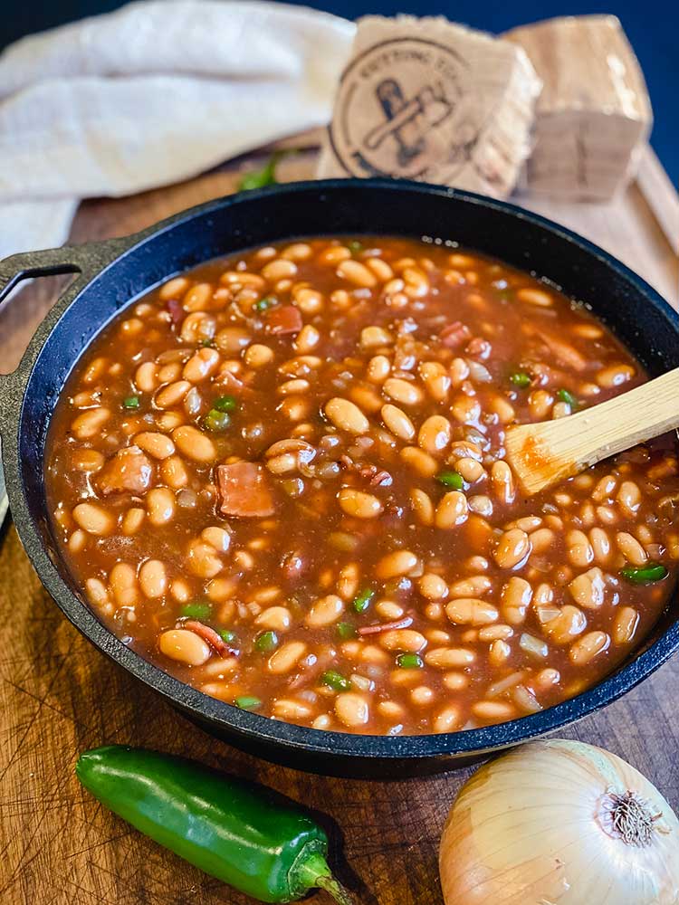 smoked baked beans resting with hickory chunk and wooden spoon