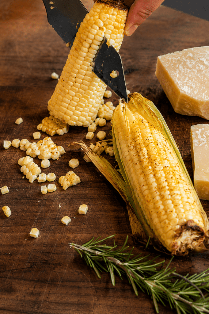 grilled corn being cut off a husk after being roasted on a grill