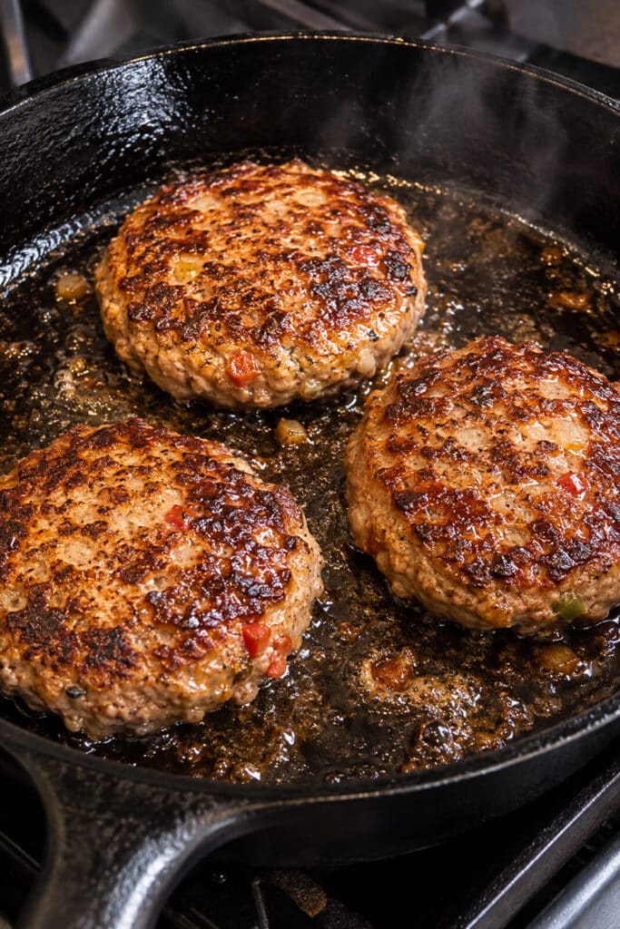 Charred meatloaf burgers frying in a cast iron pan.