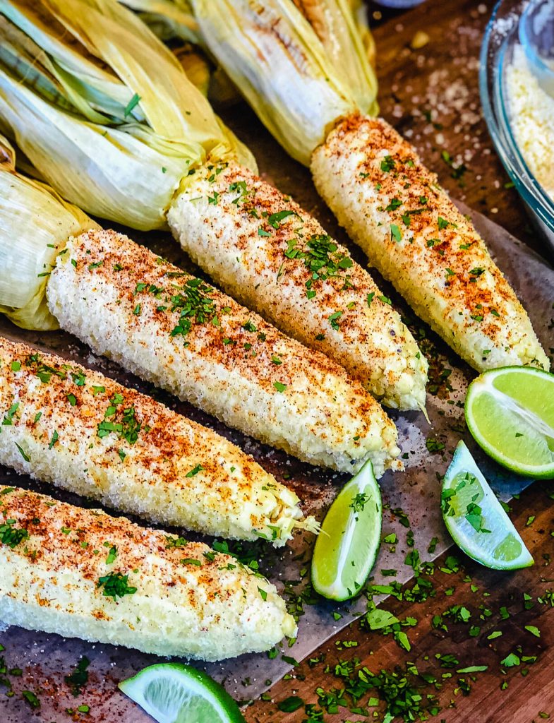 Mexican street corn on a cutting board with lime wedges and cilantro