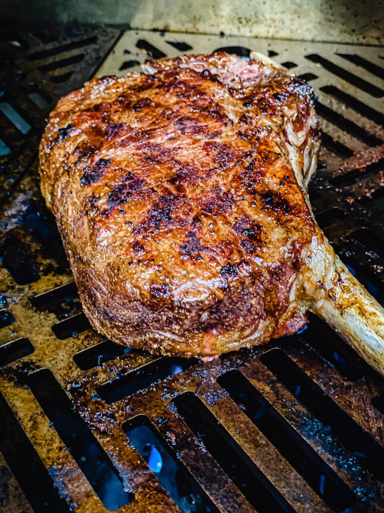 tomahawk steak being seared over a gas grill burner