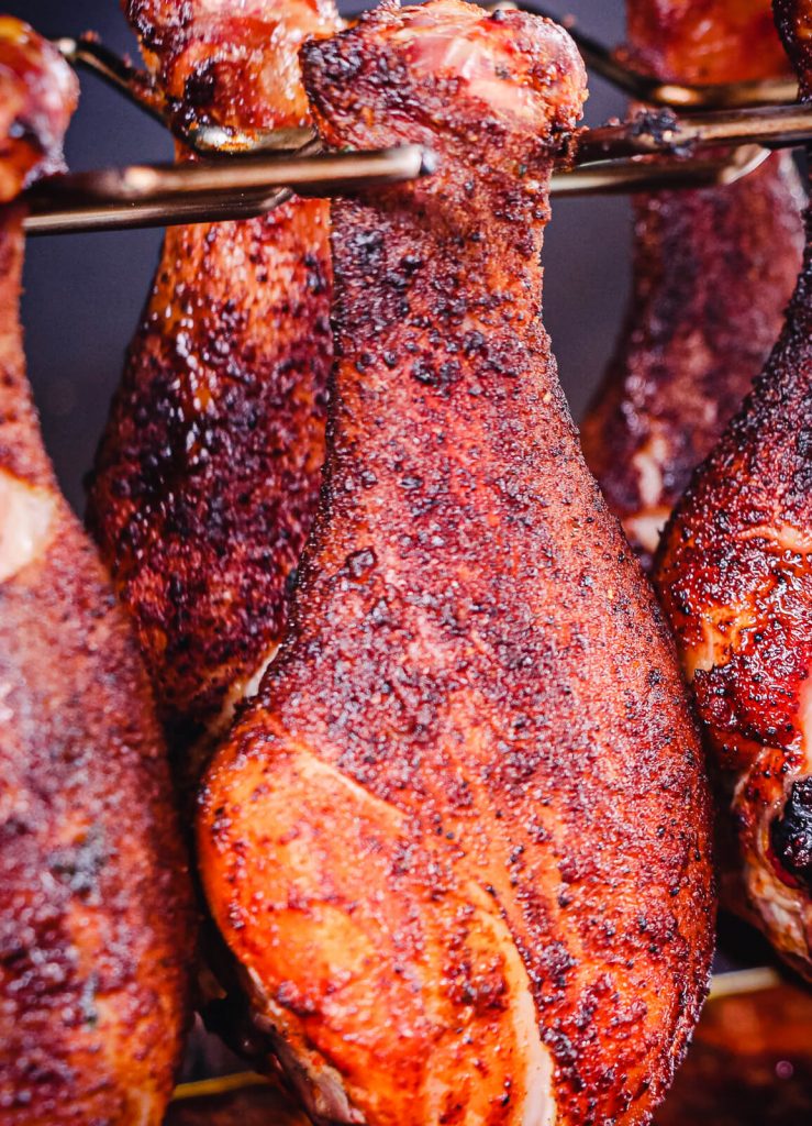 smoked chicken legs hanging on a cooking rack on a grill
