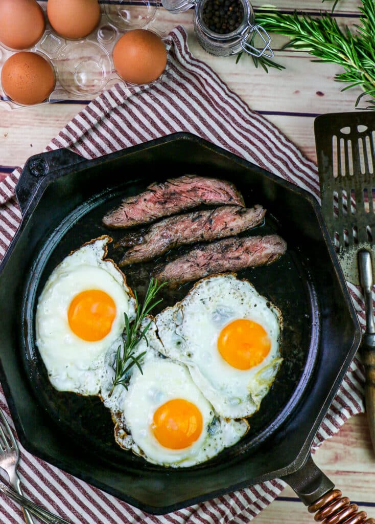 steak and eggs being cooked in a cast iron pan