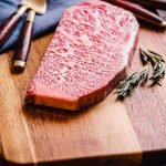 uncooked wagyu strip steak on a cutting board with utensils