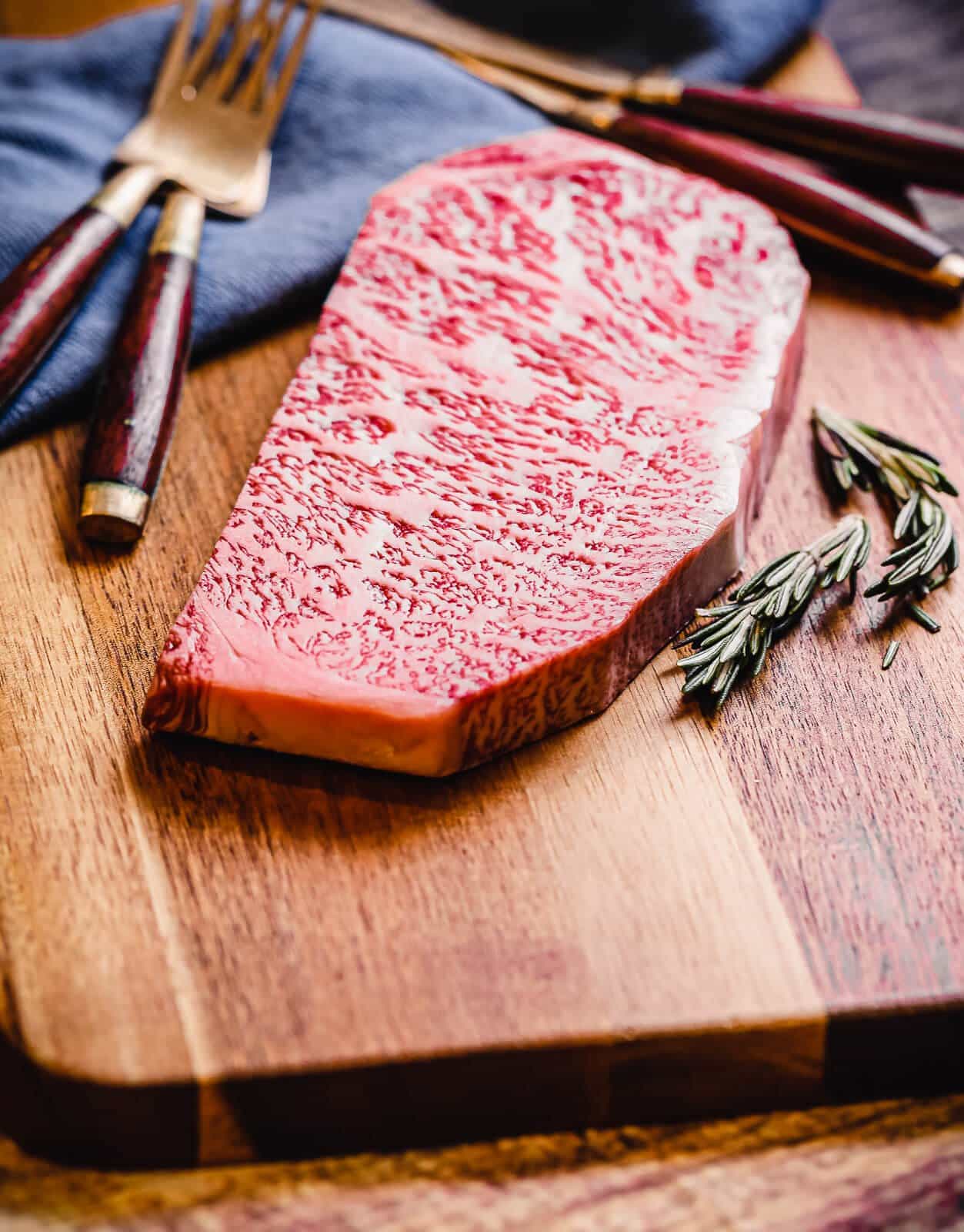 uncooked wagyu strip steak on a cutting board with utensils