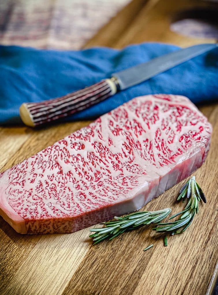 uncooked wagyu strip steak on a cutting board with a knife