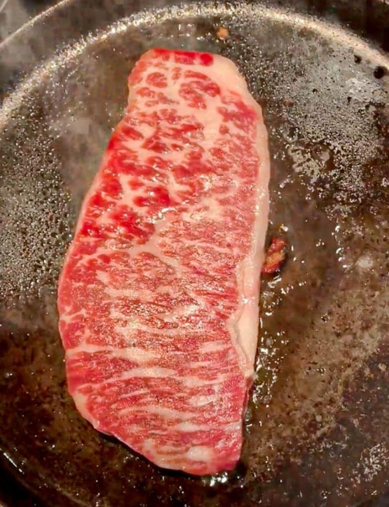 wagyu steak being cooking in a cast iron pan before being flipped