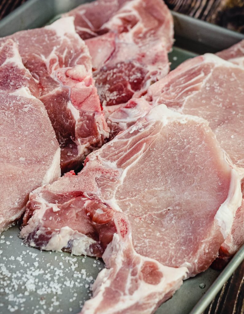 plate of uncooked pork chops seasoned with salt