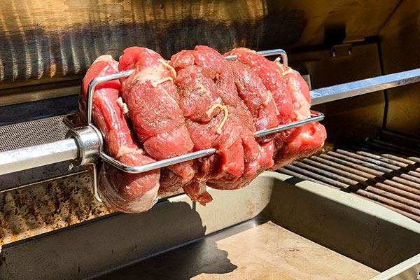 Raw lamb tied with butcher's twin on the rotisserie and cooking for the Rotisserie Boneless Leg of Lamb