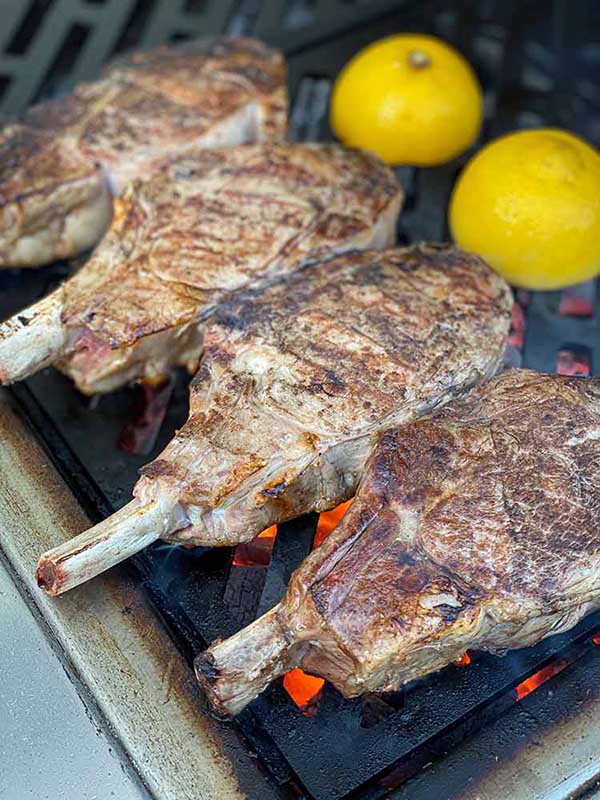 Lemons charring on the grill next to veal chops for the Veal Piccata recipe