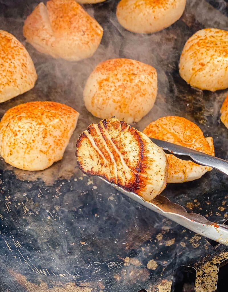 scallop being seared and flipped with tongs