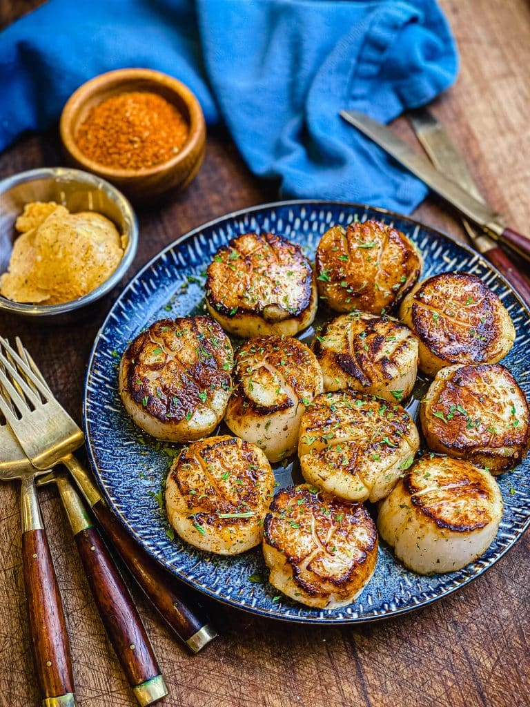 seared scallops on a blue plate with flatware