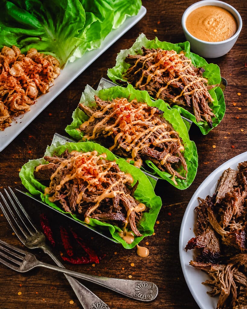 Korean style pulled pork in bibb lettuce on a wooden surface with aioli and kimchi