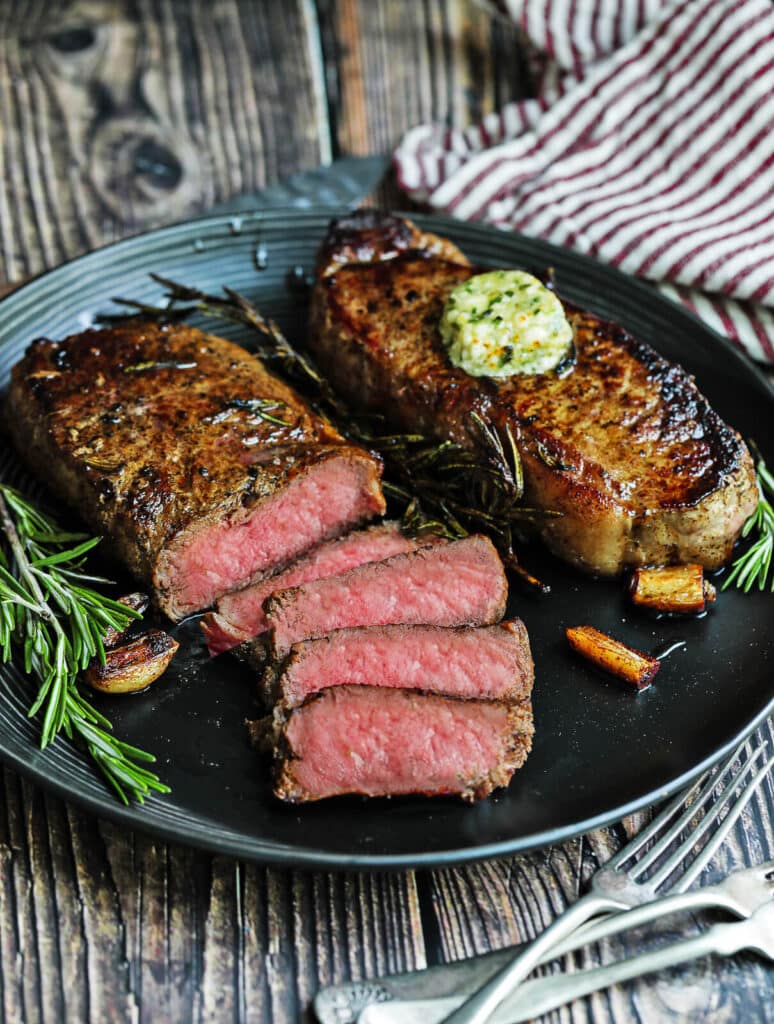 sliced pan seared strip steaks on a black plate with garlic and rosemary