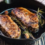 new york strip steaks with rosemary and garlic in a cast iron pan