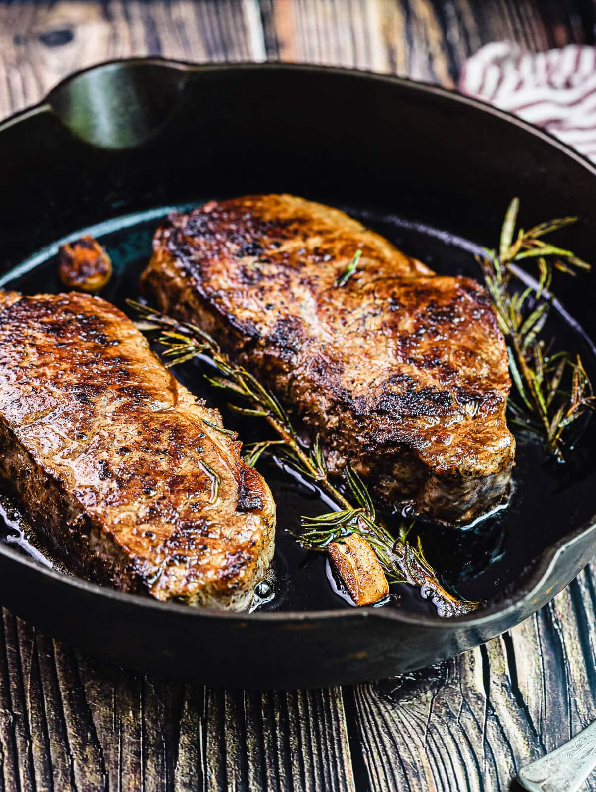new york strip steaks with rosemary and garlic in a cast iron pan