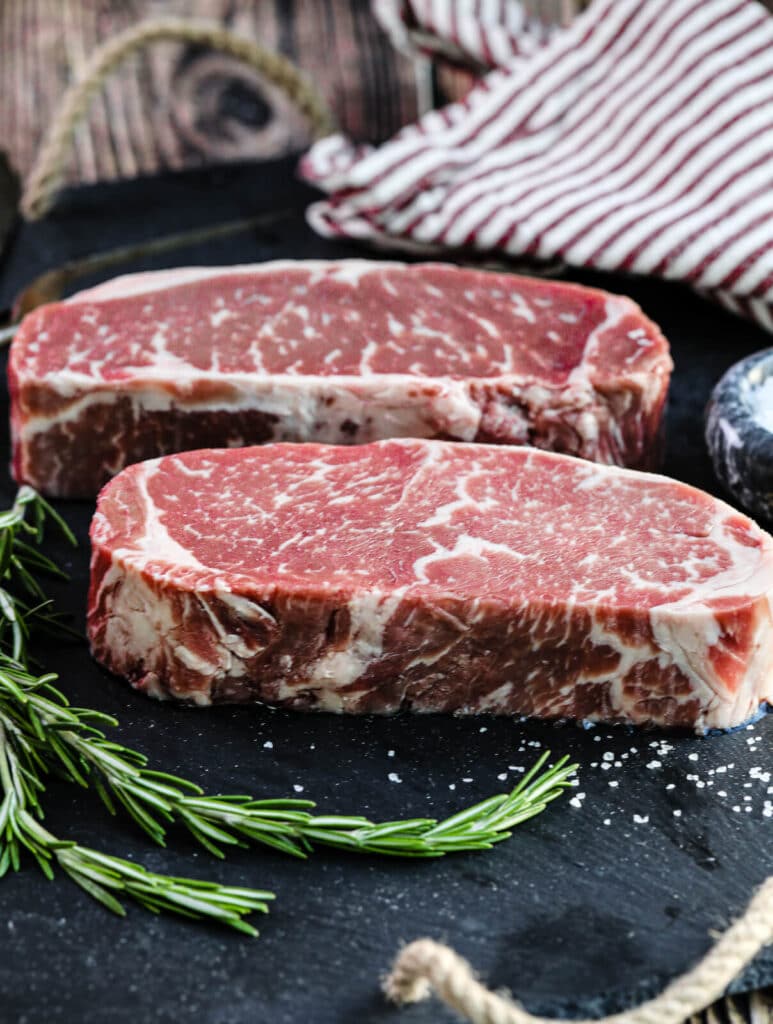 uncooked New York strip steaks sitting on a black platter