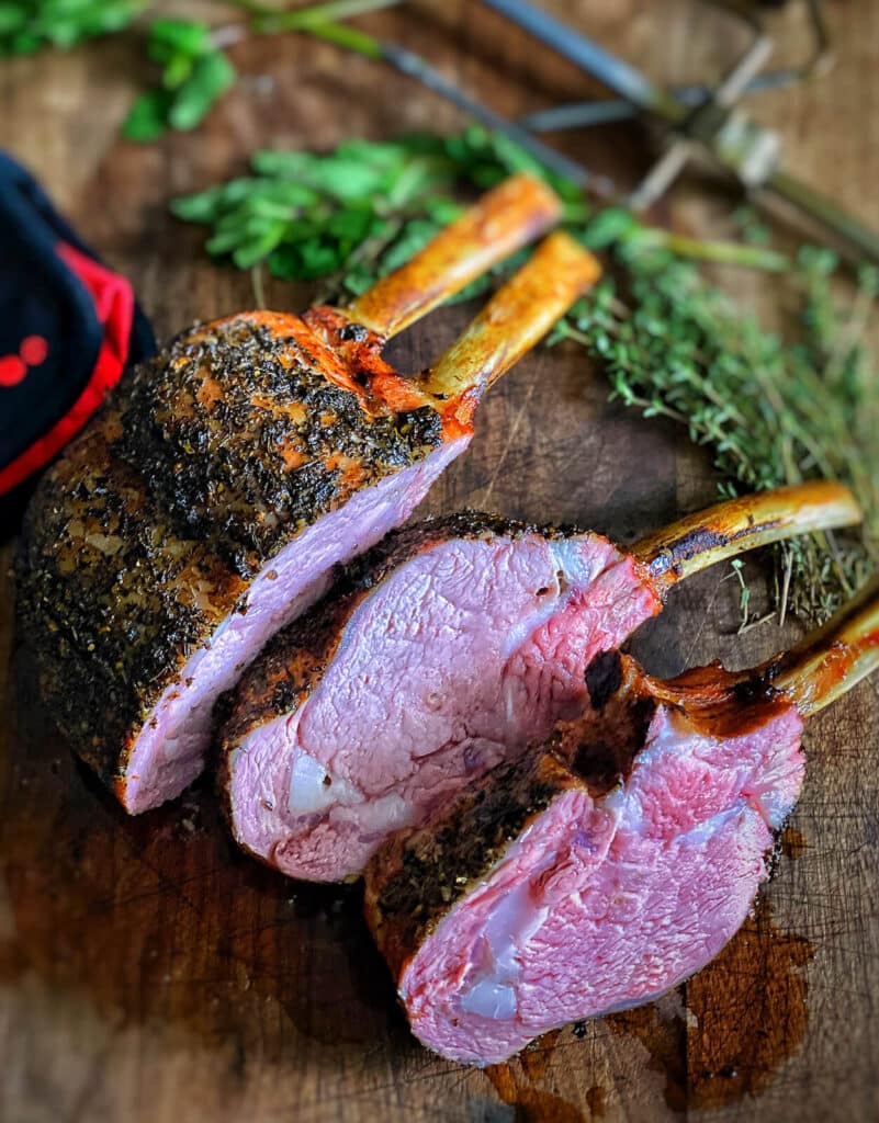 sliced rack of veal on a cutting board with herbs