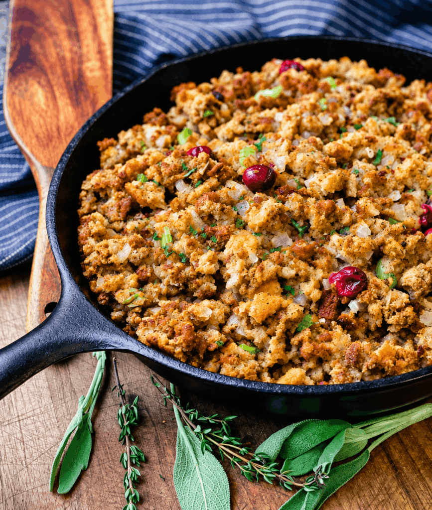 cranberry and sausage stuffing with fresh herbs on a wooden cutting board in a cast iron pan