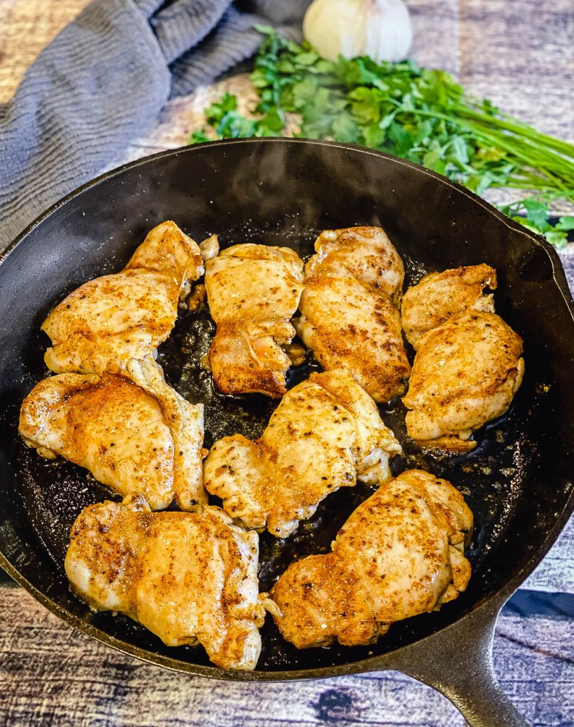 chicken thighs cooking in a cast iron pan