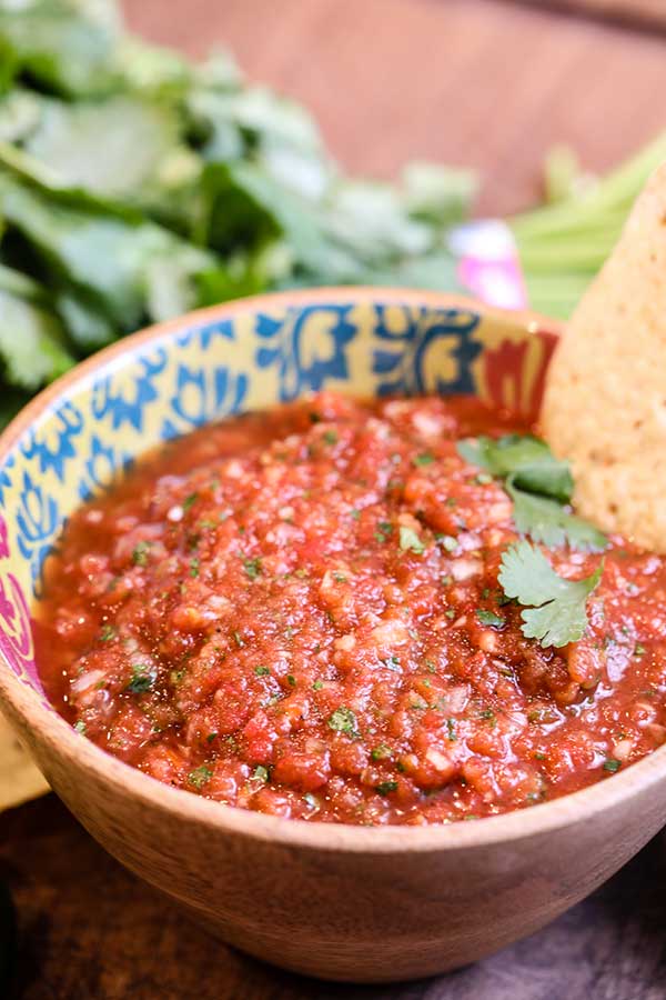 Homemade restaurant style salsa in a bowl dressed with cilantro. With chips and cilantro.