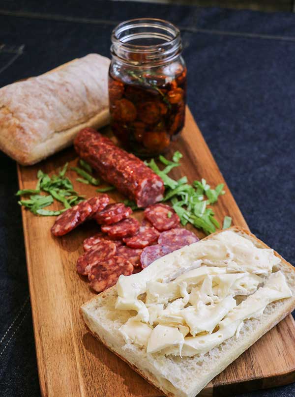 Sliced Brie on ciabatta loaf⁠—prepping spicy salami and roasted tomato sandwich