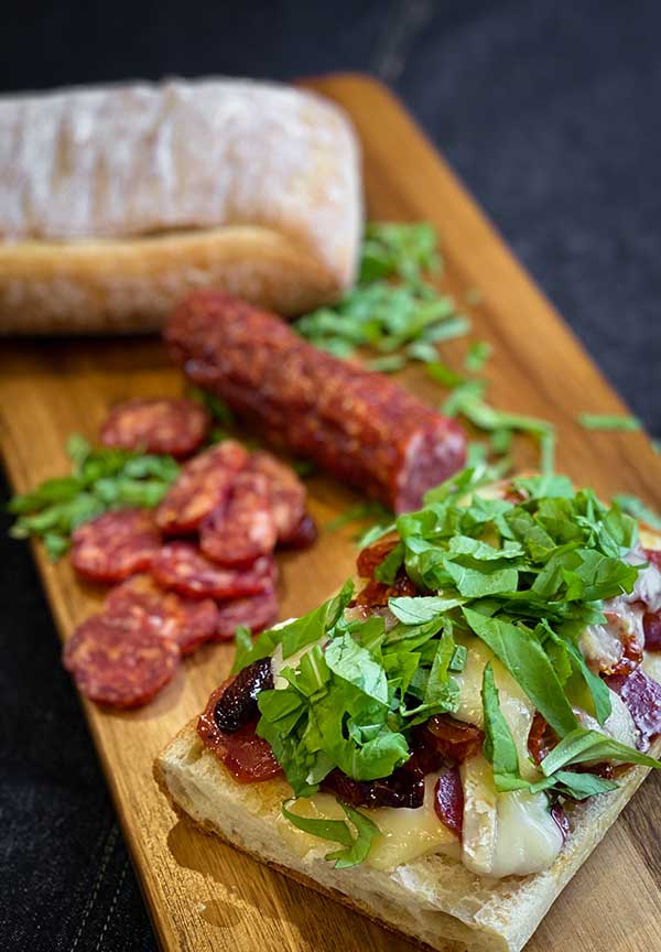 Chopped arugula, roasted tomatoes, spicy salami, and melted brie on ciabatta