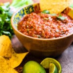 full bowl of restaurant style salsa with a chip and some limes on the countertop