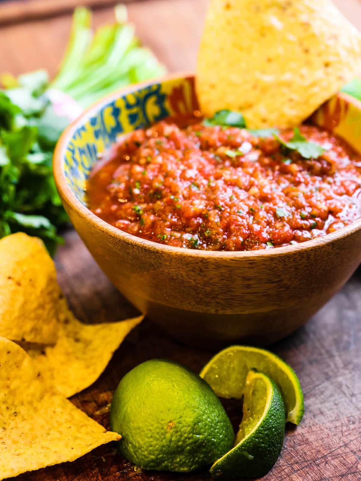 full bowl of restaurant style salsa with a chip and some limes on the countertop