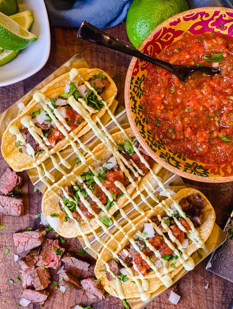 restaurant style salsa in a bowl next to street tacos and limes