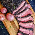 Smoked and beer braised corned beef, sliced on a cutting board with red potatoes