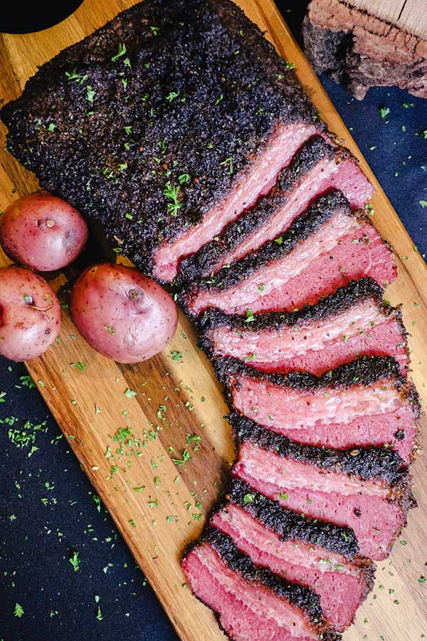 Smoked and beer braised corned beef, sliced on a cutting board with red potatoes