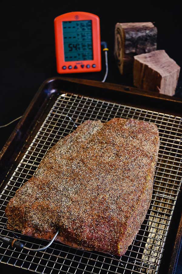 Seasoned corned beef on a rack with a mult-channel thermometer and hickory wood in the background