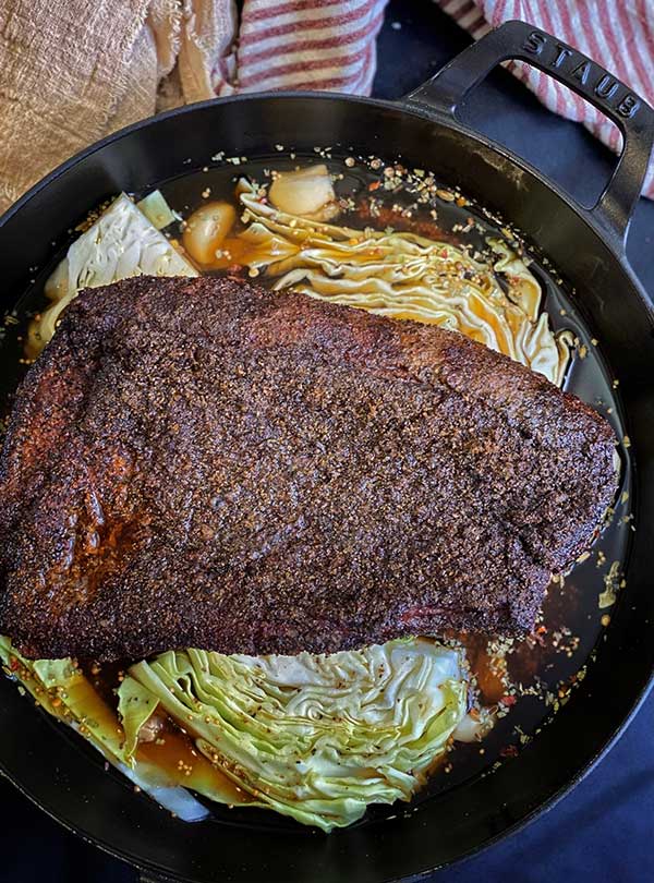Smoked corned beef on a bed of cabbage semi-circles and potatoes with beer braise in an oven-safe pan