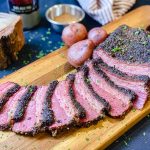 A cutting board with slices of corned beef and potatoes in front of a block of hickory wood and spices