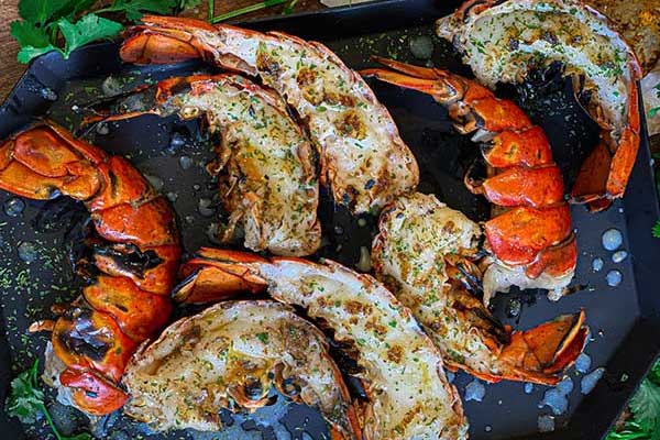 Grilled lobster tail halves plated with view of the seared lobster flesh that makes this method tasty and the shells that hold the sauce while grilling