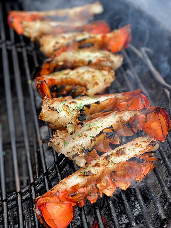 Grilling lobster tail halves with shell side facing heat to poach in chipotle butter sauce
