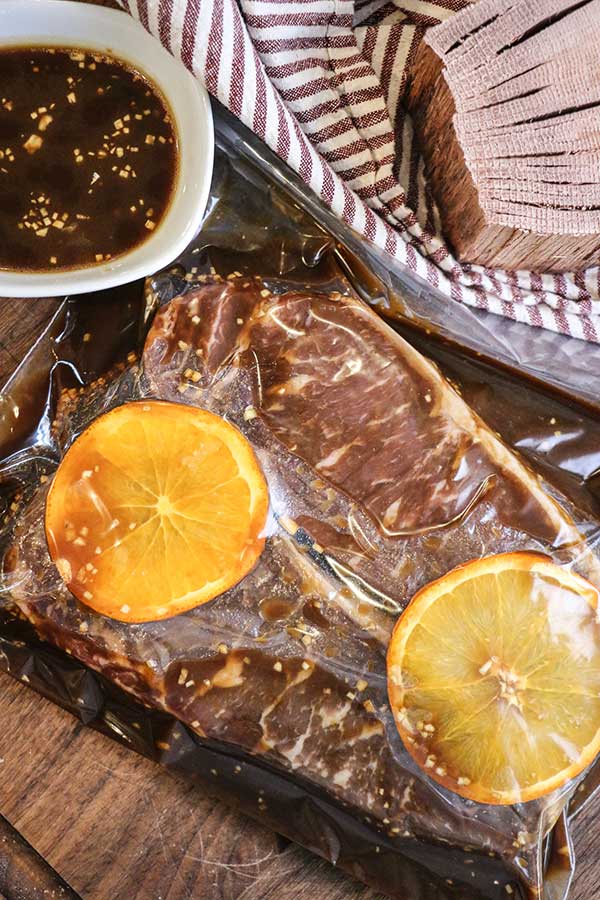 Strip steaks marinating in a bag with orange slices and bourbon marinade