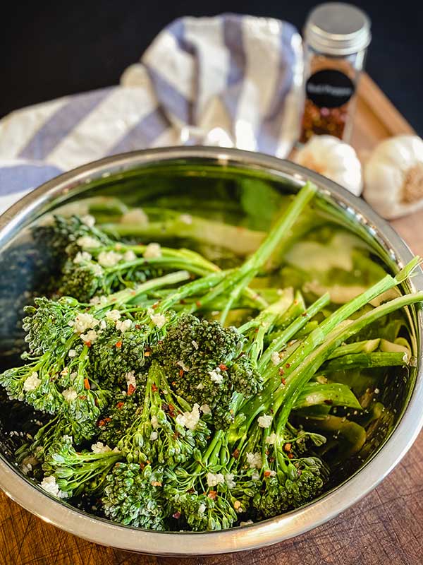 broccolini stalks in a bowl with minced garlic and olive oil