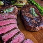 perfectly grilled New York strip steak sliced and ready to serve, on a cutting board with bok choy