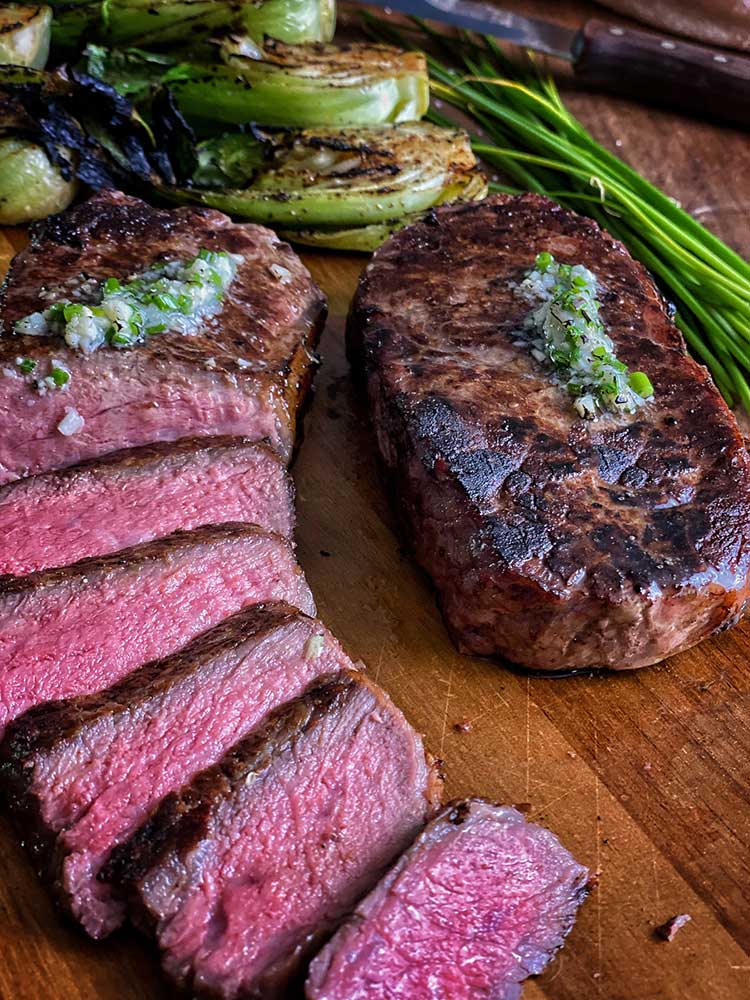 perfectly grilled New York strip steak sliced and ready to serve, on a cutting board with bok choy
