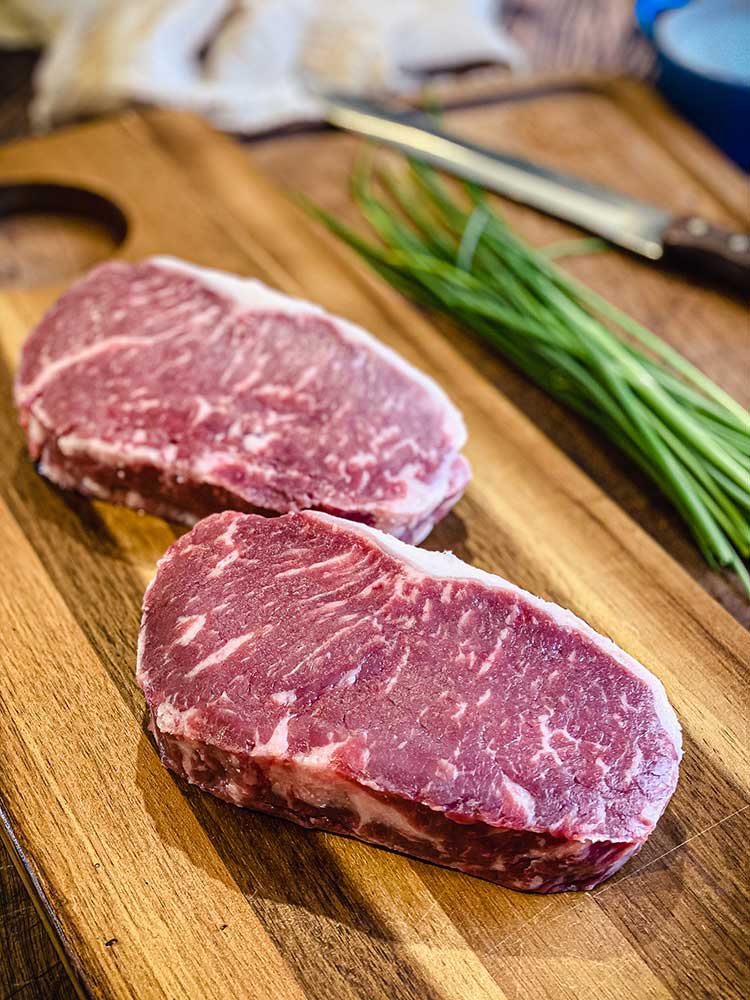 uncooked New York strip steak on the counter at room temperature