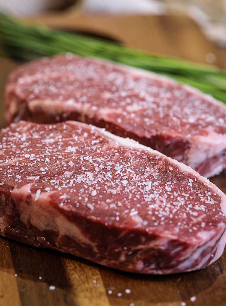 uncooked and beautifully marbled New York strip steak coated in olive oil and coarse sea salt