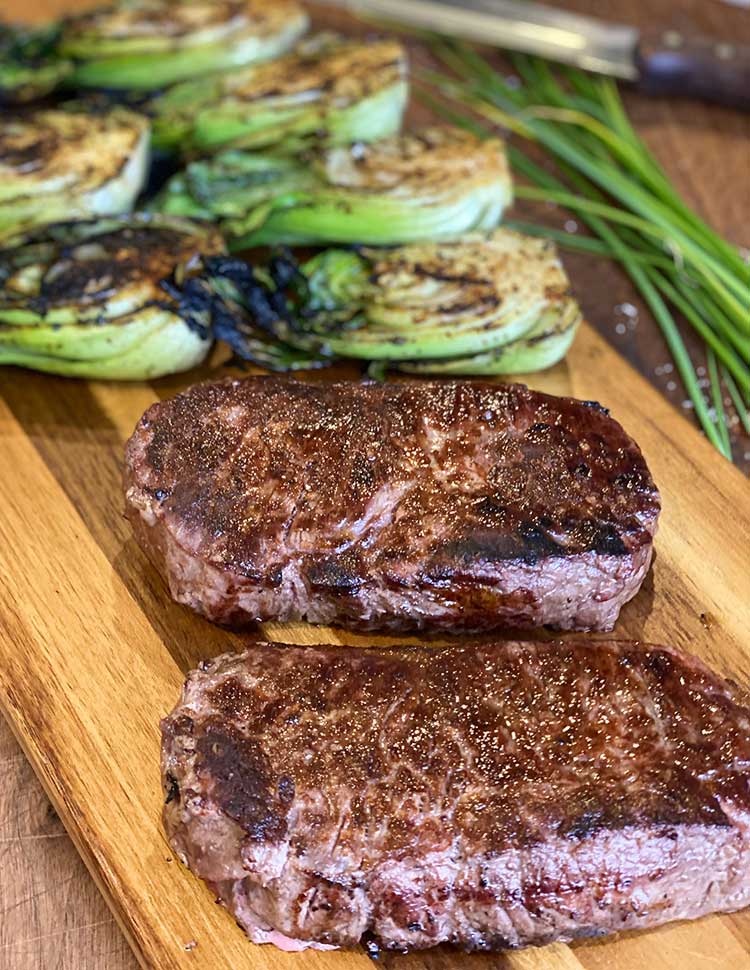 grillowany New York strip steak na desce do krojenia z grillowanym bok choy