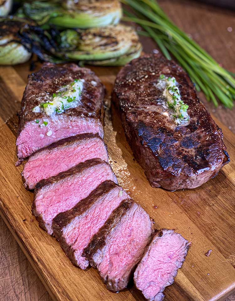 Perfectly grilled New York strip steak sliced on a cutting board