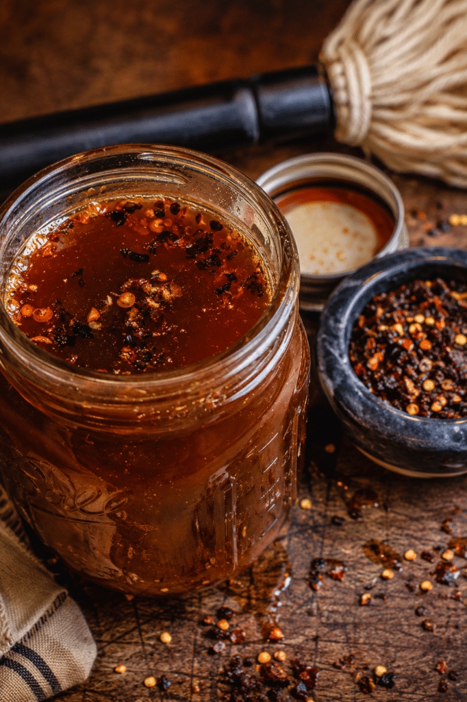 A jar of homemade, Eastern Carolina mop sauce with some red pepper flakes and a bbq mop.