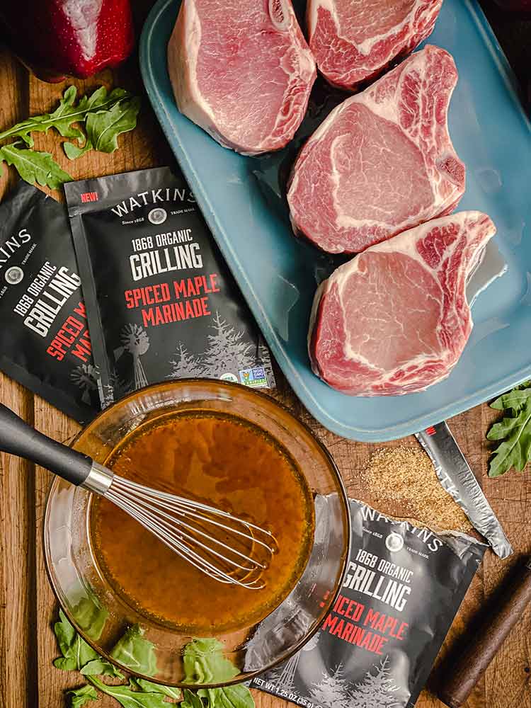 Watkins spiced maple marinade packets, a bowl of marinade, and pork chops ready for marinade.