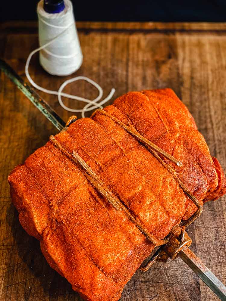 pork roast on a spit and then coated with yellow mustard and seasoned on all sides