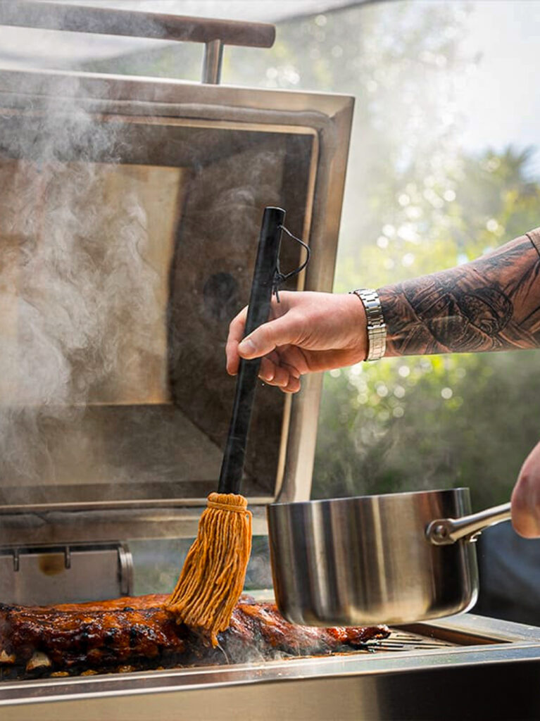 BBQ mop drizzling East Carolina mop sauce on a rack of baby back ribs on the grill