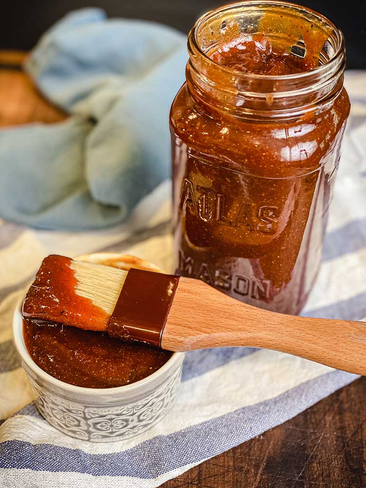 jar of homemade barbecue sauce with brush and bowl